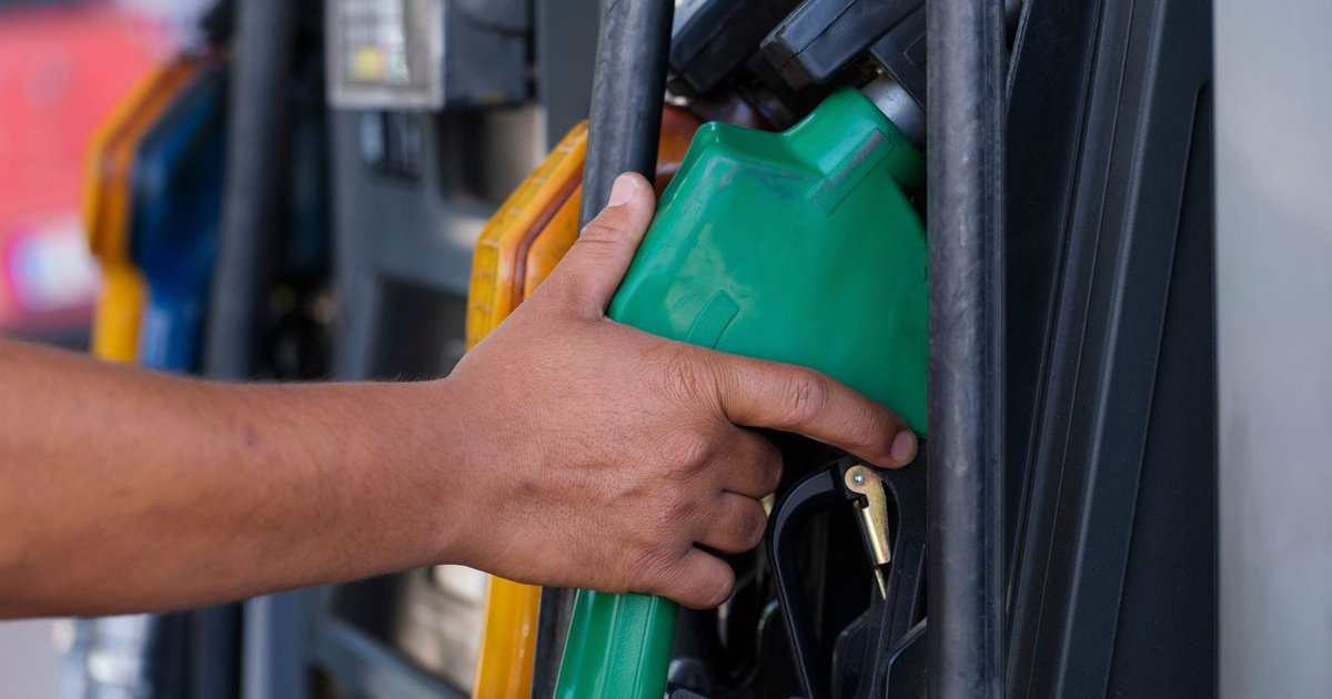 Surtidor de gasolinera con la manguera en la mano de una persona repostando combustible